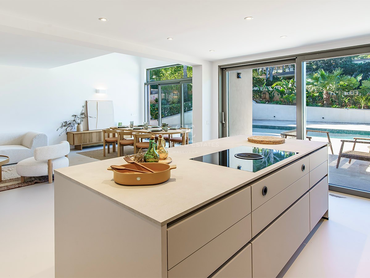Interior luminoso y moderno con isla de cocina, comedor, sofás y grandes ventanales que dan a una piscina.