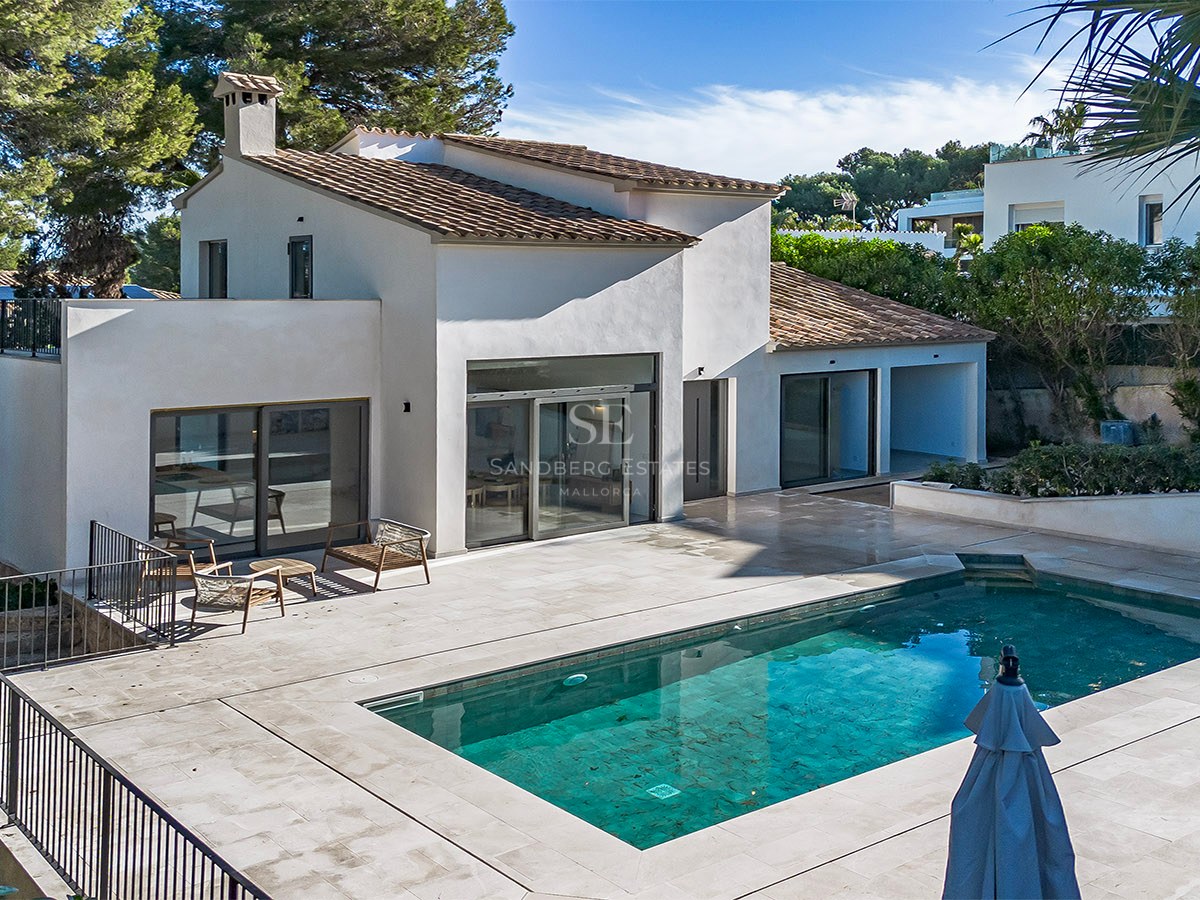 Villa blanca de estilo mediterráneo con una piscina rectangular azul y una amplia terraza de piedra bajo el sol.