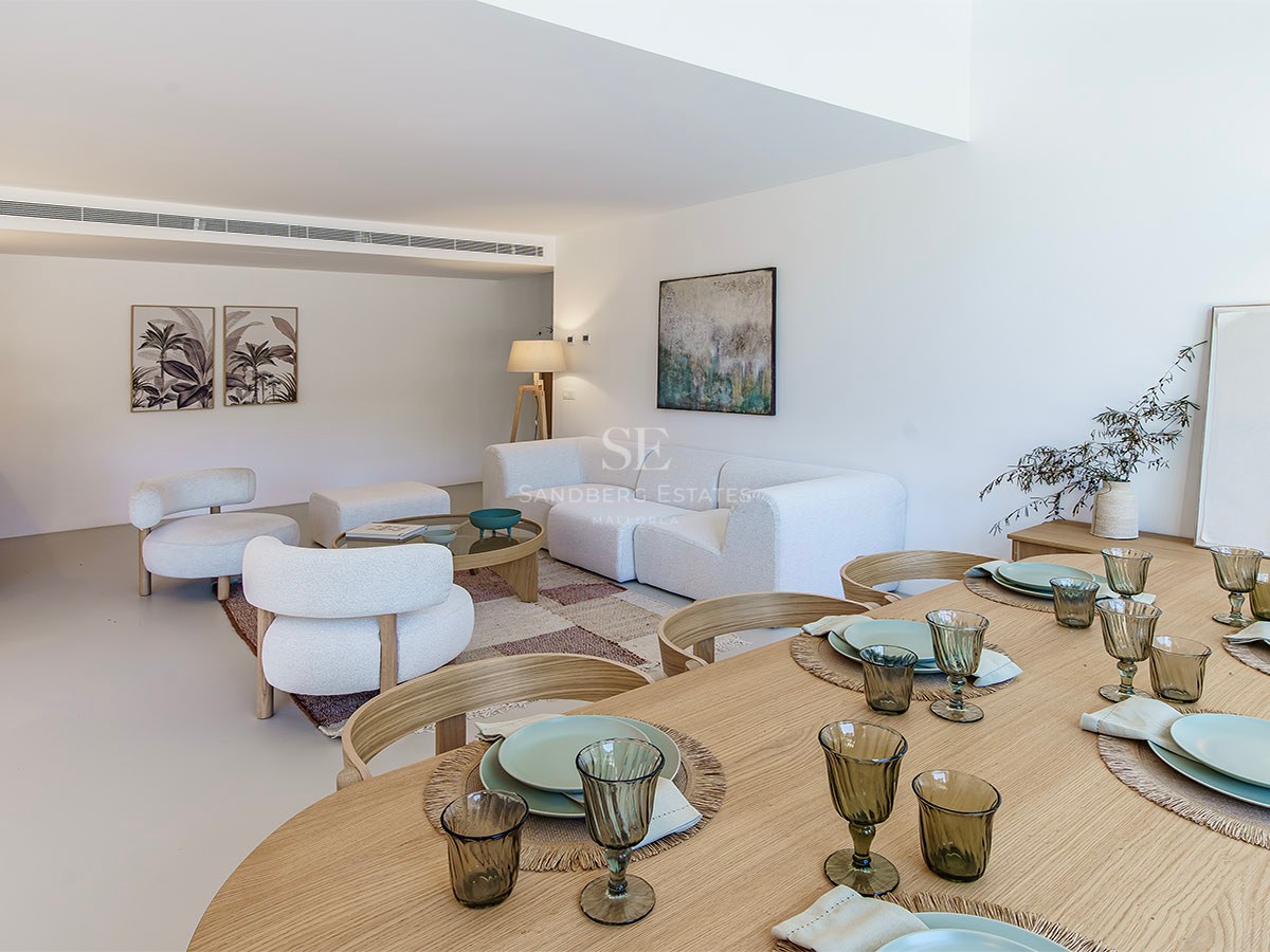 Amplio salón-comedor con sofás de tela bouclé blanca, mesa de comedor de madera y decoración minimalista.