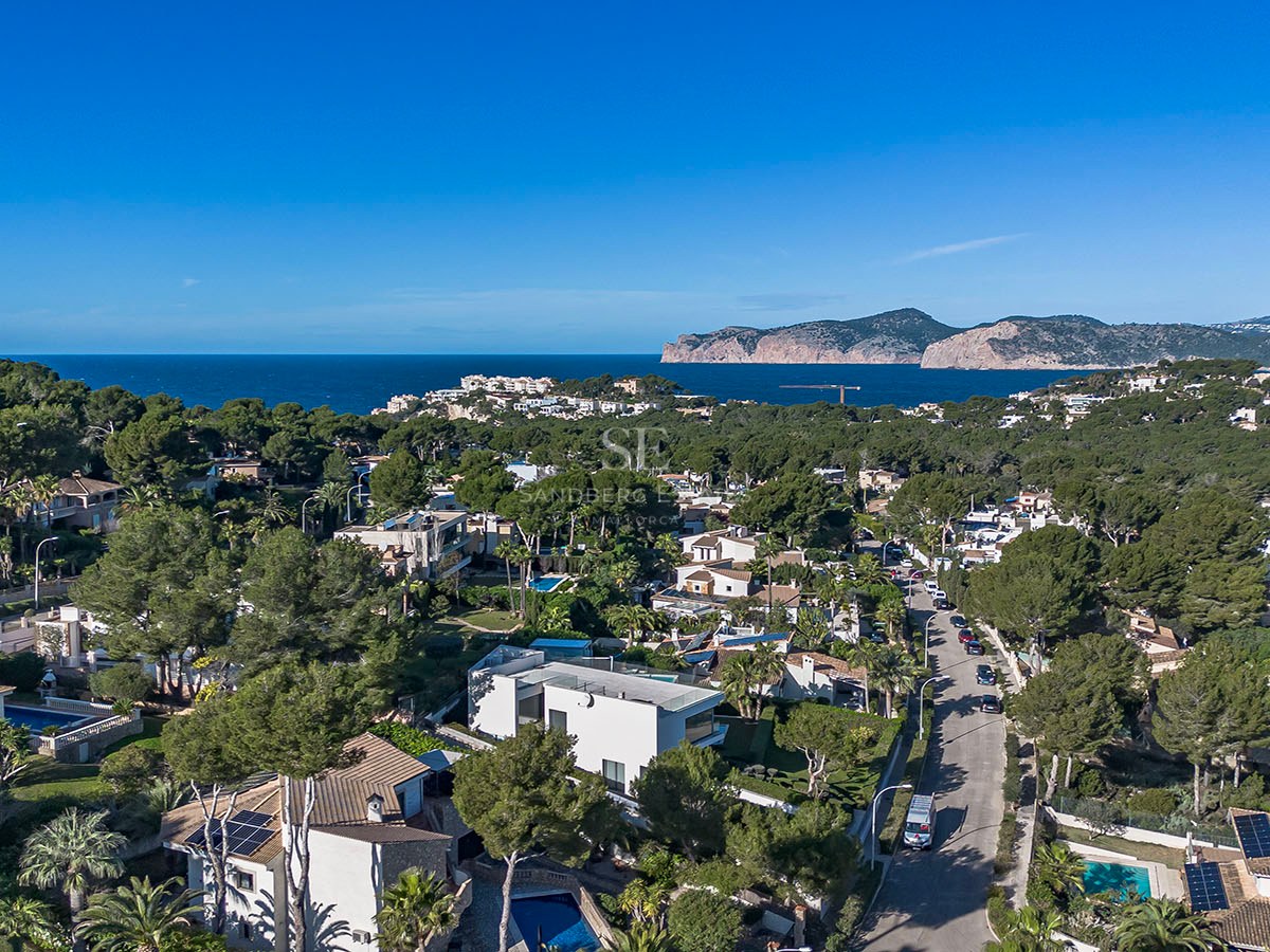 Vista de dron de un vecindario costero con casas de lujo, pinos y el mar Mediterráneo al fondo.