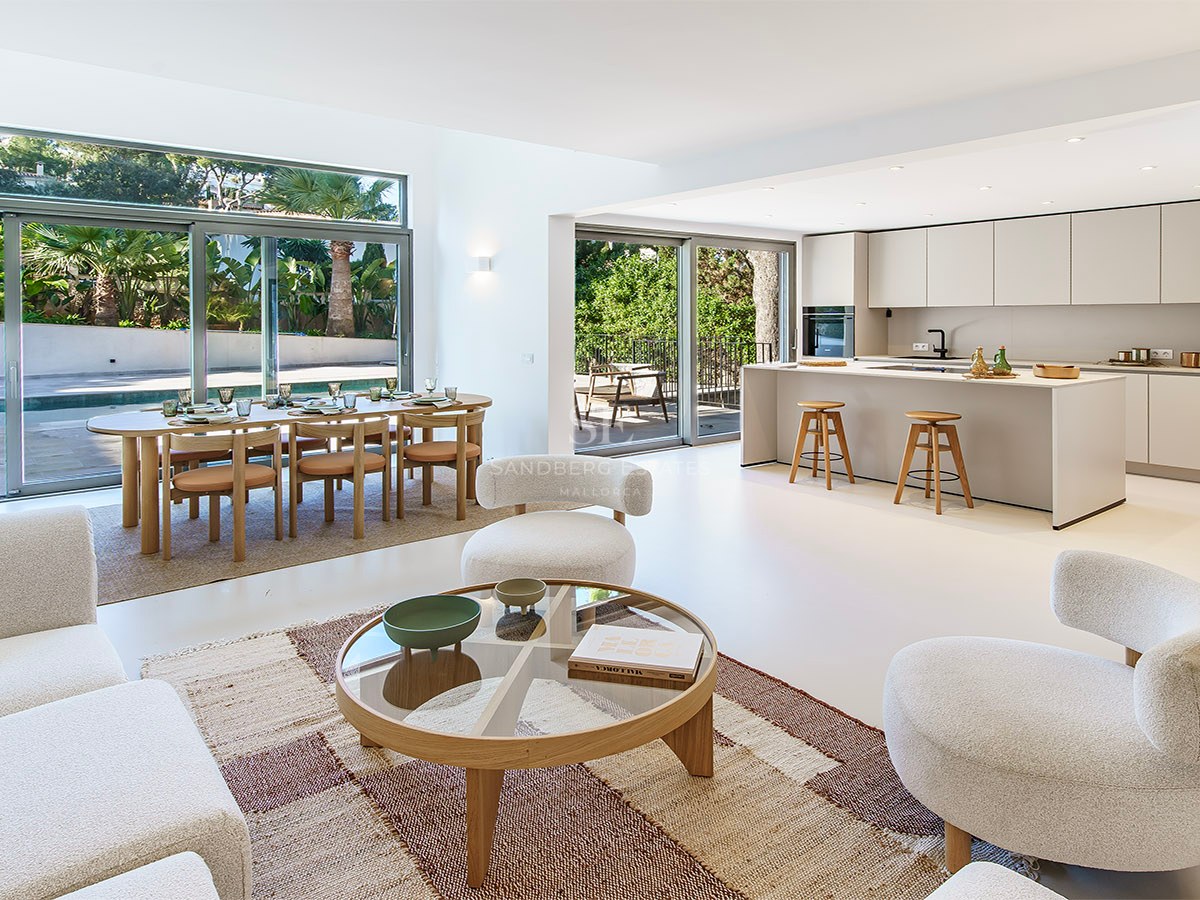 Amplio salón de concepto abierto con sofás blancos, comedor de madera y cocina moderna con vistas a la piscina.
