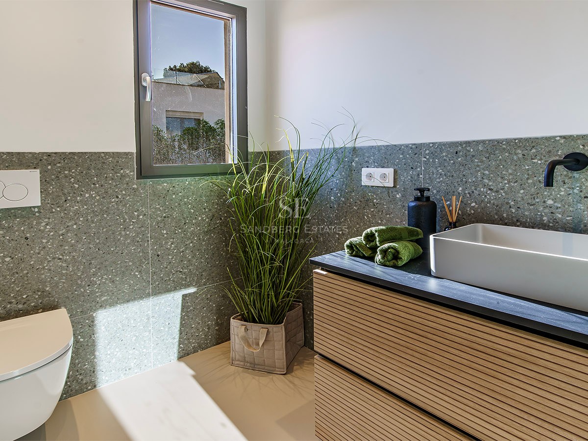 Baño minimalista con lavabo de sobreponer, grifo negro, inodoro suspendido y paredes de terrazo verde.
