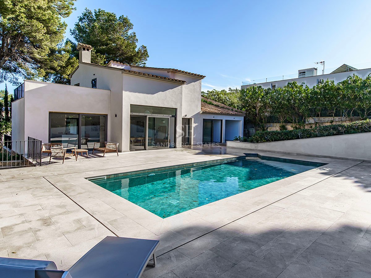 Villa blanca moderna con piscina rectangular turquesa y terraza de piedra rodeada de pinos.