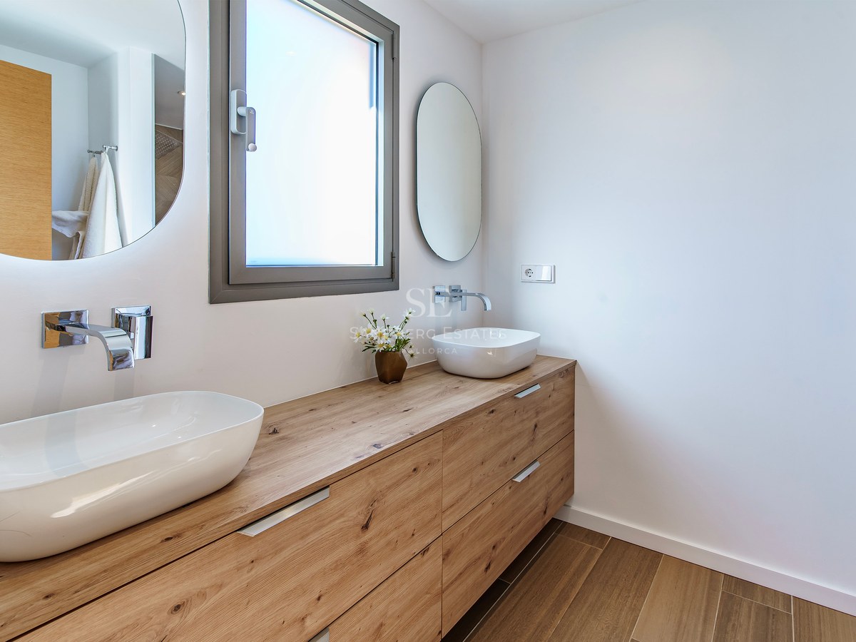 Salle de bain moderne avec un long meuble en bois, deux vasques blanches et des miroirs circulaires rétroéclairés.