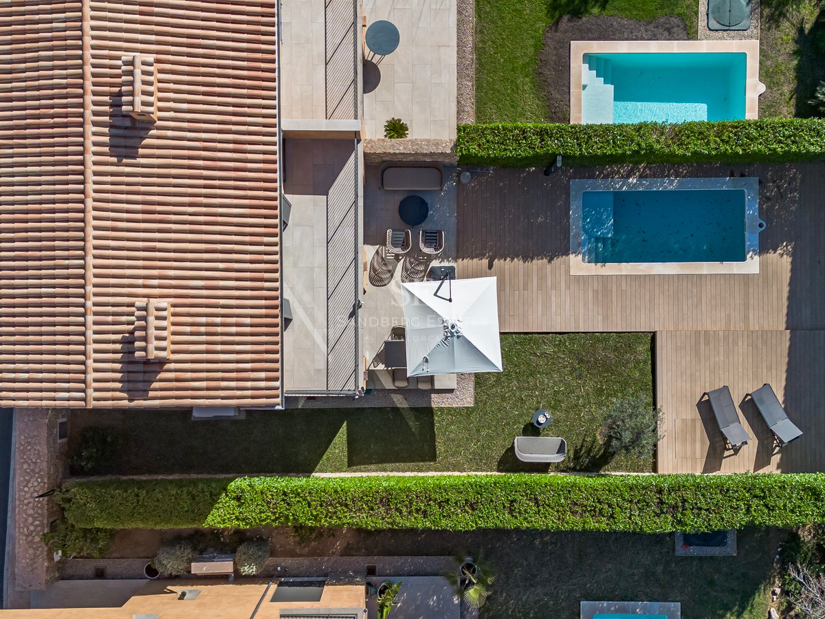 Vue d'oiseau d'une villa méditerranéenne avec toit en terre cuite, terrasse en bois, piscine et pelouse verdoyante.
