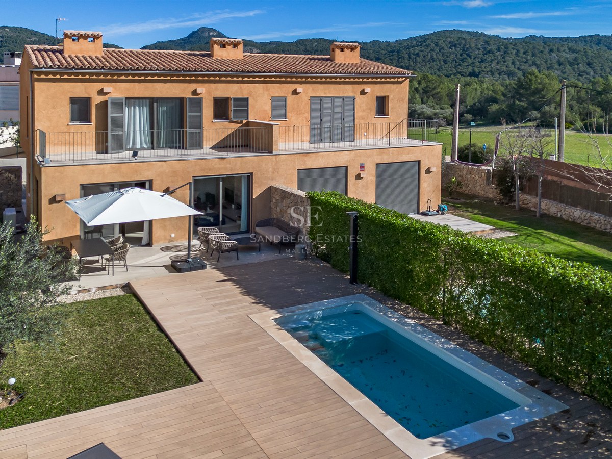Vue aérienne d'une villa ocre avec piscine, terrasse en bois, jardin et montagnes en arrière-plan.
