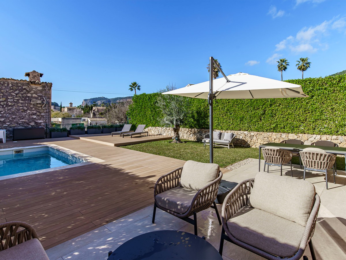 Piscine moderne avec terrasse en bois, mobilier d'extérieur élégant et haies verdoyantes sous un ciel bleu.