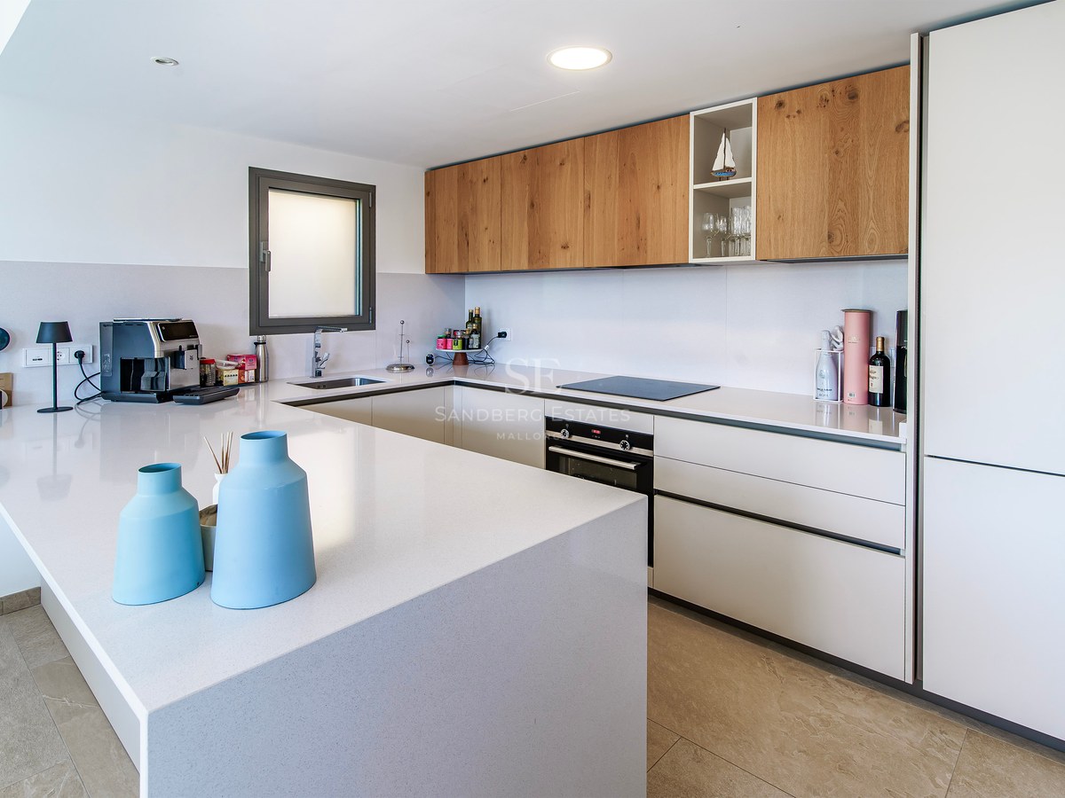 Cuisine blanche moderne avec meubles hauts en bois, grand îlot blanc et appareils encastrés.