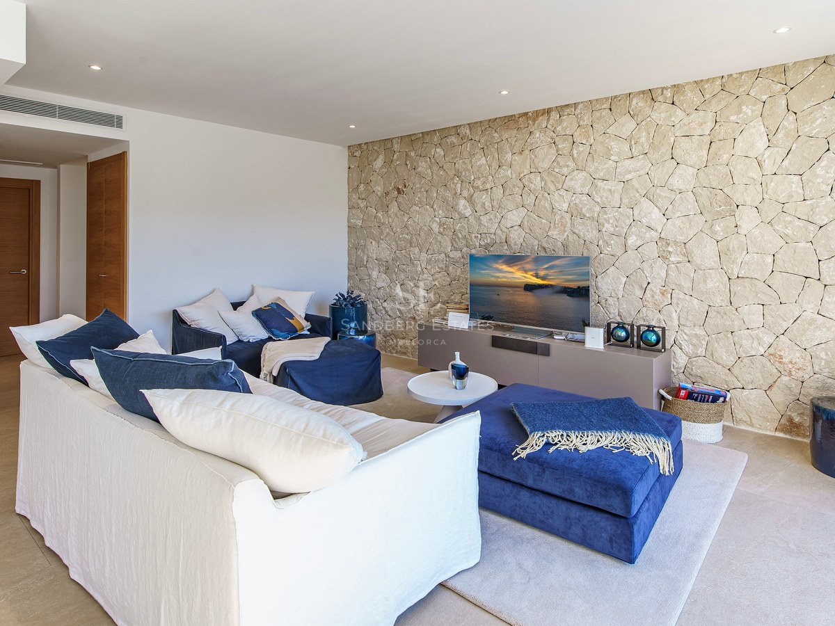 Salon contemporain avec canapé blanc, poufs bleu marine et mur en pierre naturelle texturée avec télévision.