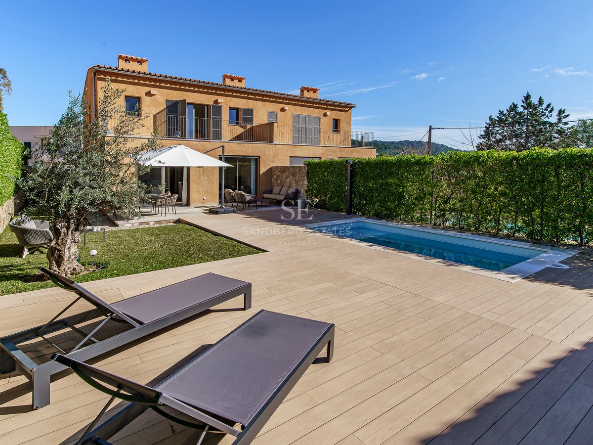 Piscine moderne et terrasse en bois avec transats à côté d'une villa en terre cuite sous un ciel bleu clair.