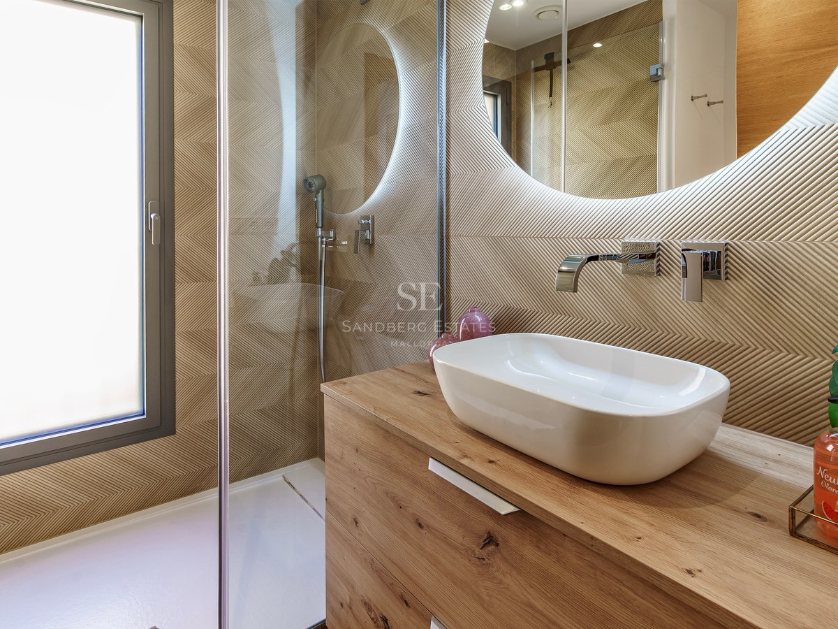 Salle de bain avec vasque à poser sur bois, miroir rond rétroéclairé et paroi de douche en verre.