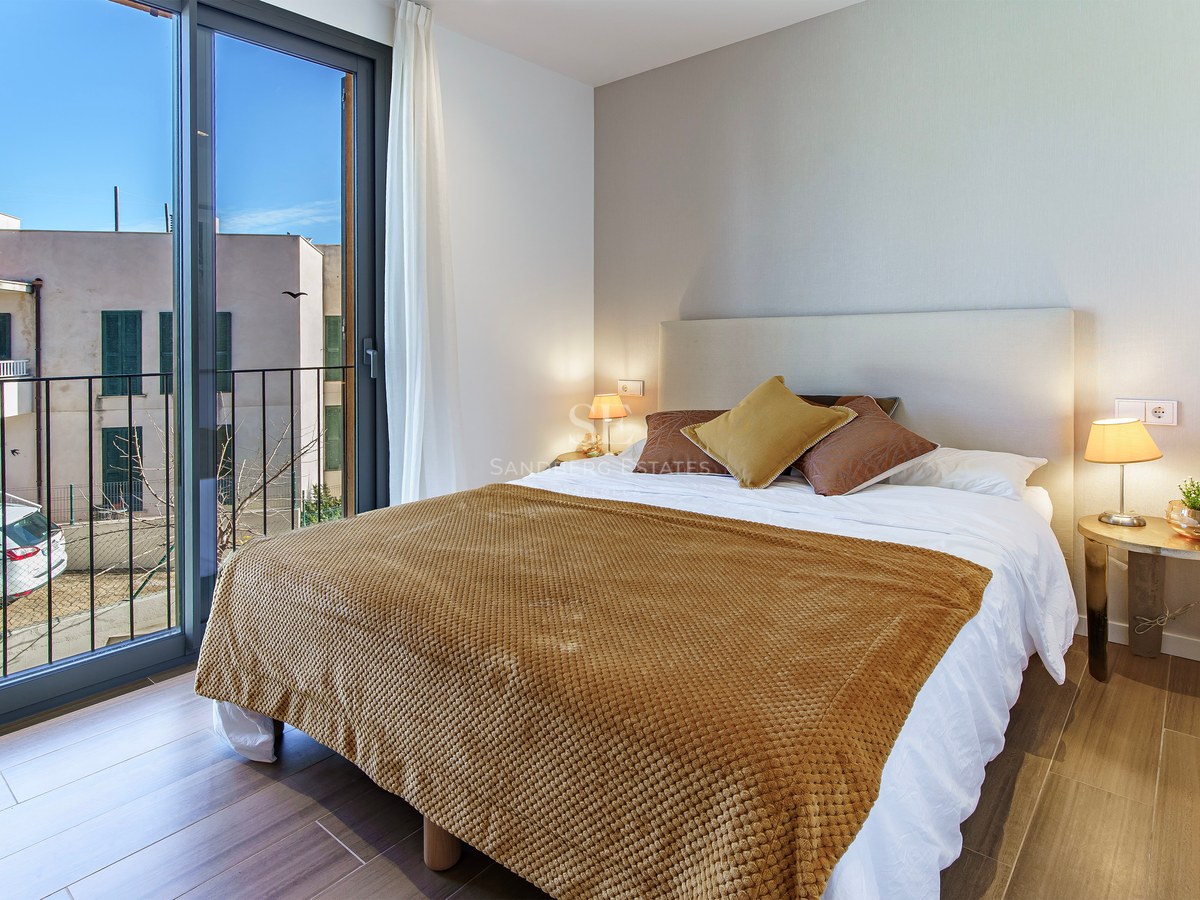Chambre lumineuse avec un lit double, un jeté jaune ocre, une grande fenêtre et un balcon.