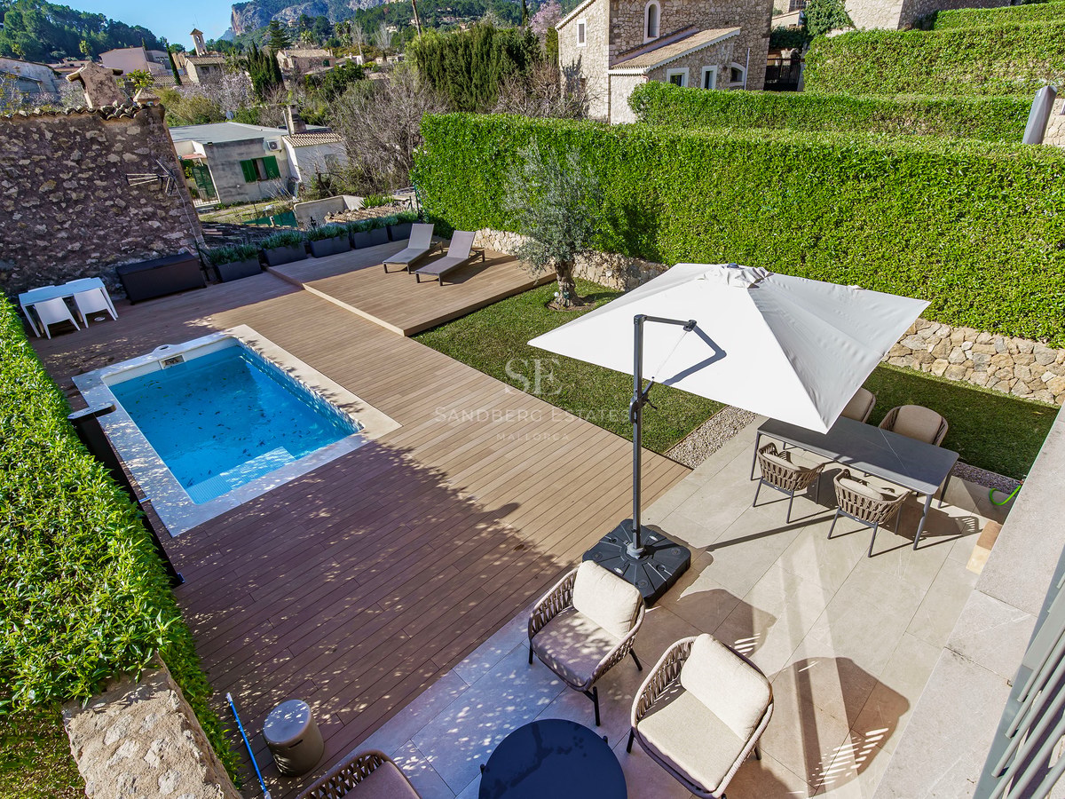 Vue de dessus d'une piscine rectangulaire, d'une terrasse en bois, d'une pelouse et d'un coin repas extérieur entourés de haies.