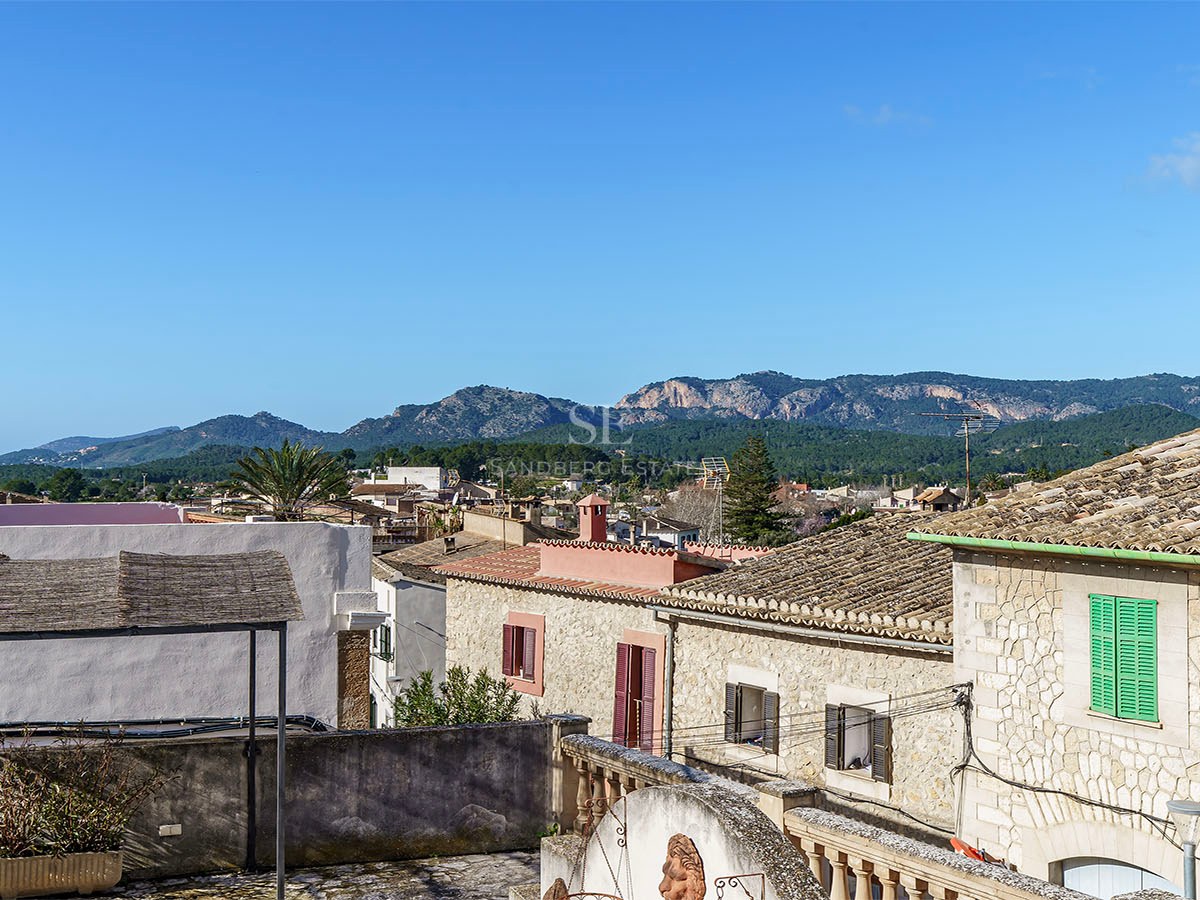 Utsikt från en stenterrass över terrakottatak och gröna berg under en klarblå himmel på Mallorca.