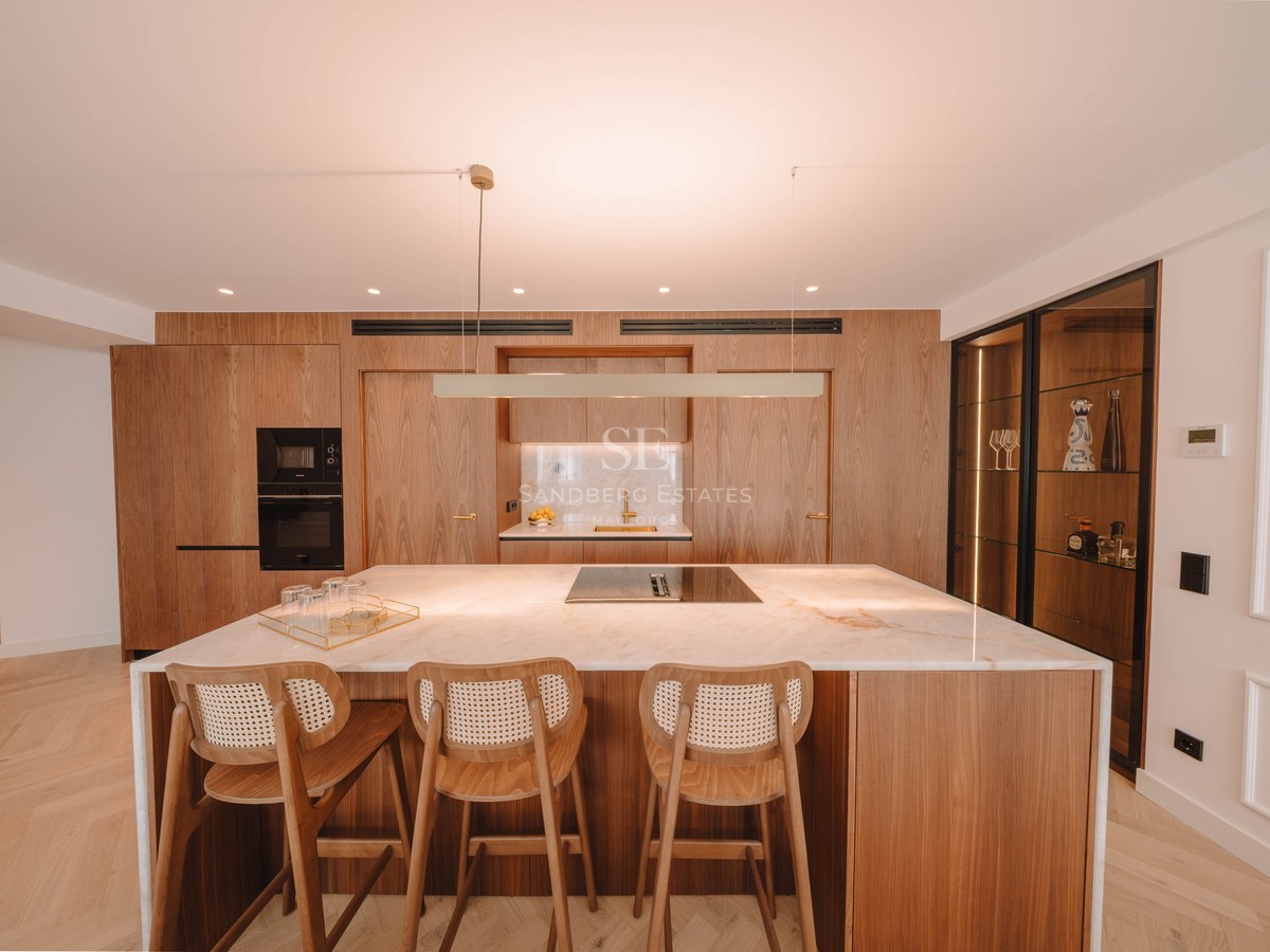 Modern kitchen featuring a white marble island, wood bar stools, and floor-to-ceiling warm wood cabinetry.