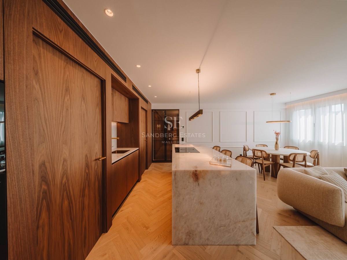 Modern open-plan kitchen featuring a large marble island, walnut cabinetry, and herringbone wood floors.