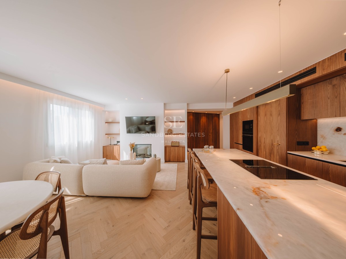 Bright open-concept living area with a beige sofa, marble kitchen island, and warm wood flooring.