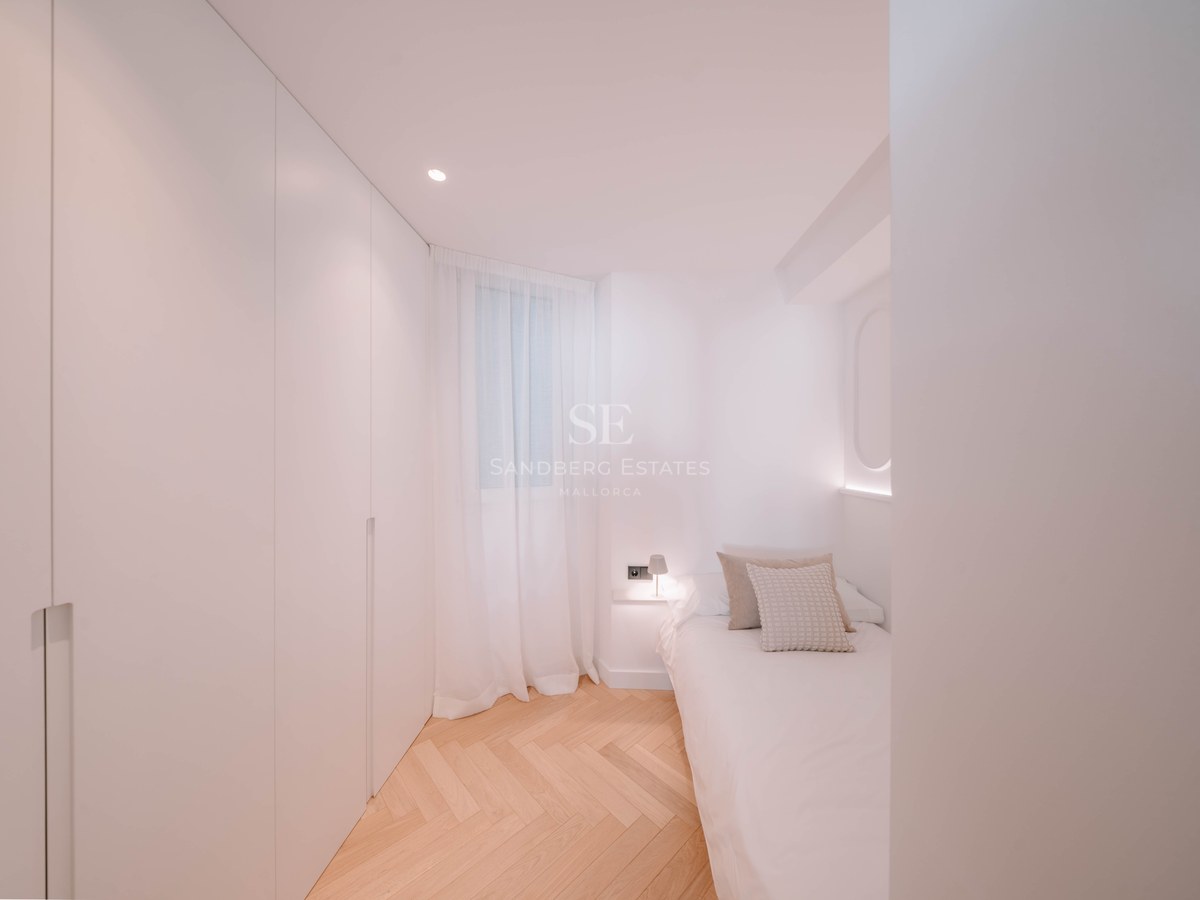 Bright bedroom featuring white built-in closets, herringbone wood floors, and a single bed with soft lighting.