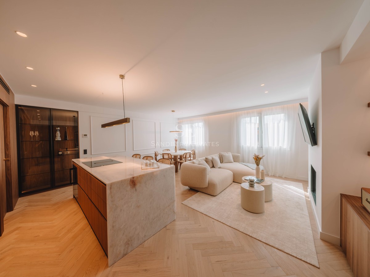 Bright open-plan living room with a large marble kitchen island, curved beige sofa, and herringbone wood floors.