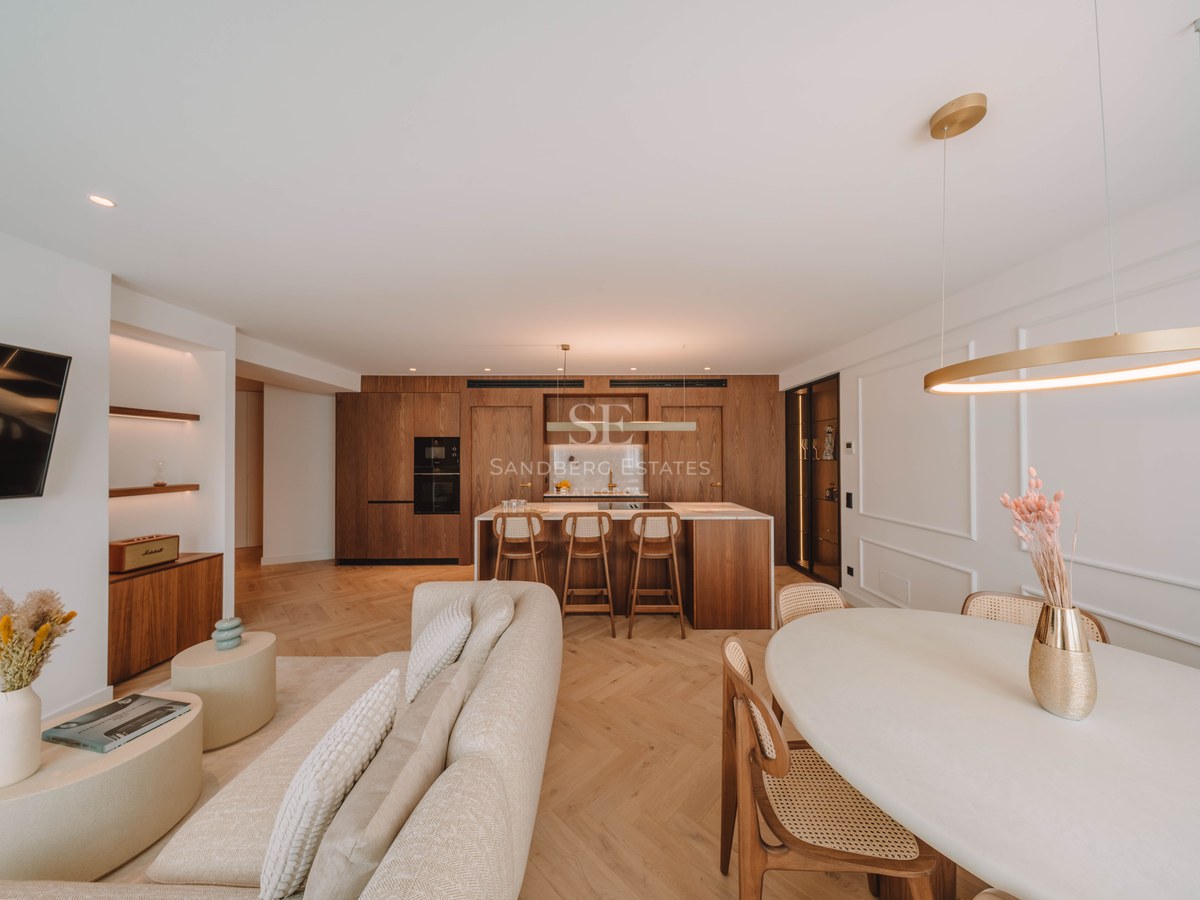 Spacious luxury living room featuring a beige sofa, herringbone wood floors, and an integrated natural wood kitchen.