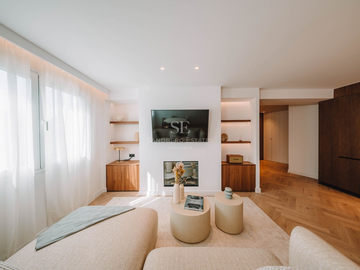 Bright living room featuring a wall-mounted TV, electric fireplace, herringbone wood floors, and cream sofas.