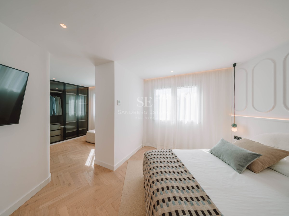 Bright master bedroom featuring herringbone wood floors, a large bed with pillows, and a glass-front walk-in closet.