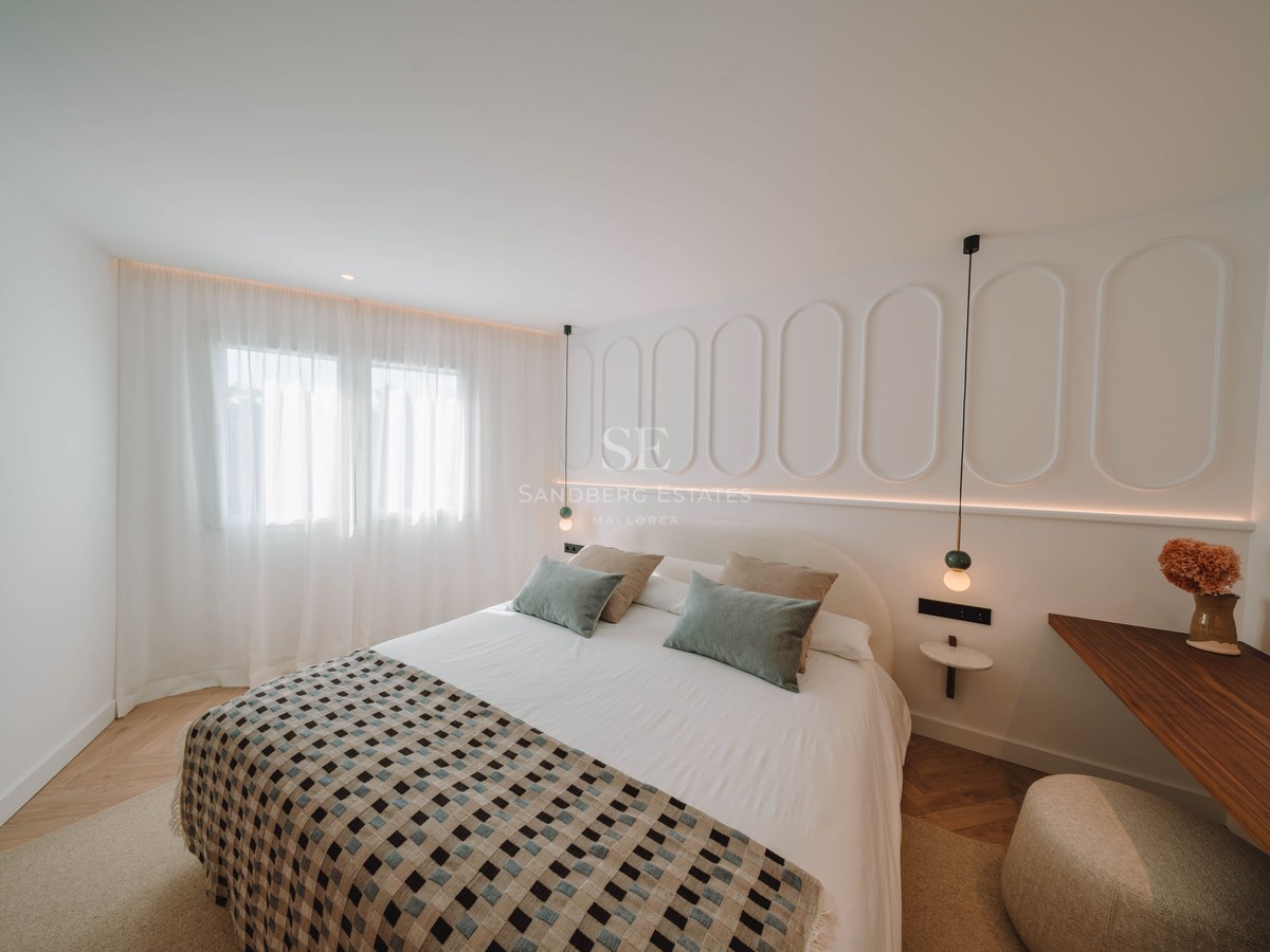 Bright bedroom featuring a large bed, white walls with oval molding, and elegant herringbone wood flooring.