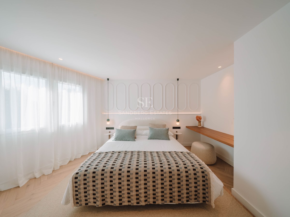 A bright, modern bedroom featuring a patterned bedspread, white paneled headboard wall, and herringbone wood flooring.