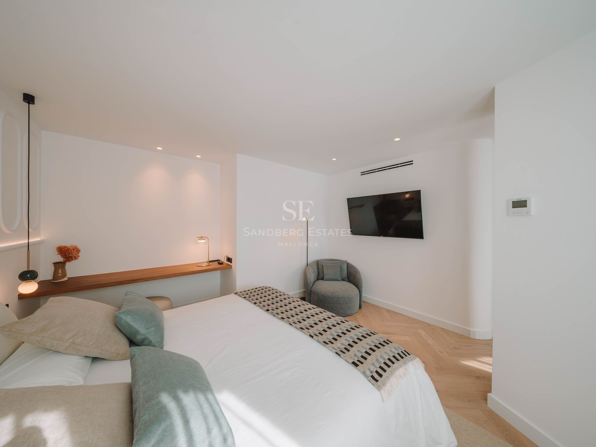 Modern bedroom featuring a white bed with sage green pillows, wooden shelf, and herringbone wood flooring.