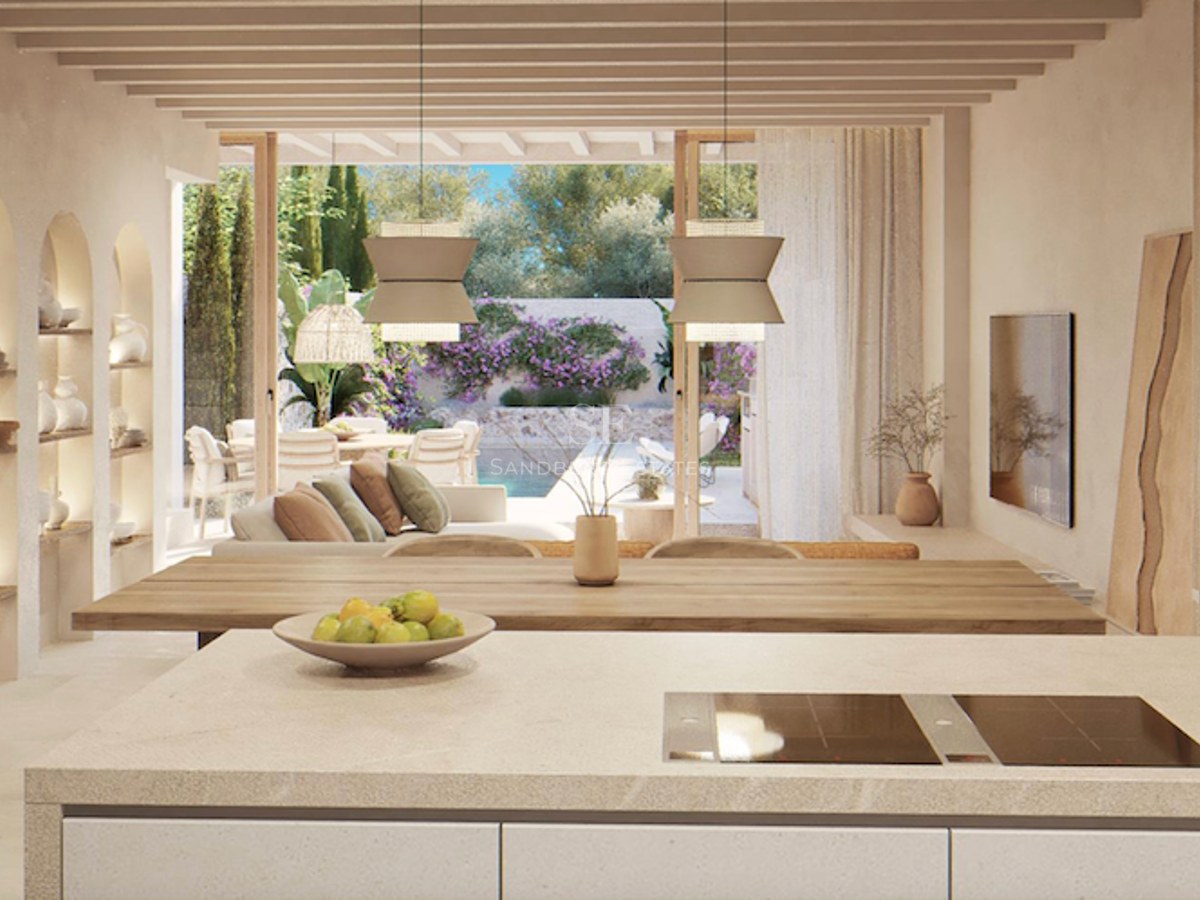 Open-plan space with a kitchen island, wooden beams, and views of a terrace with a pool and garden.