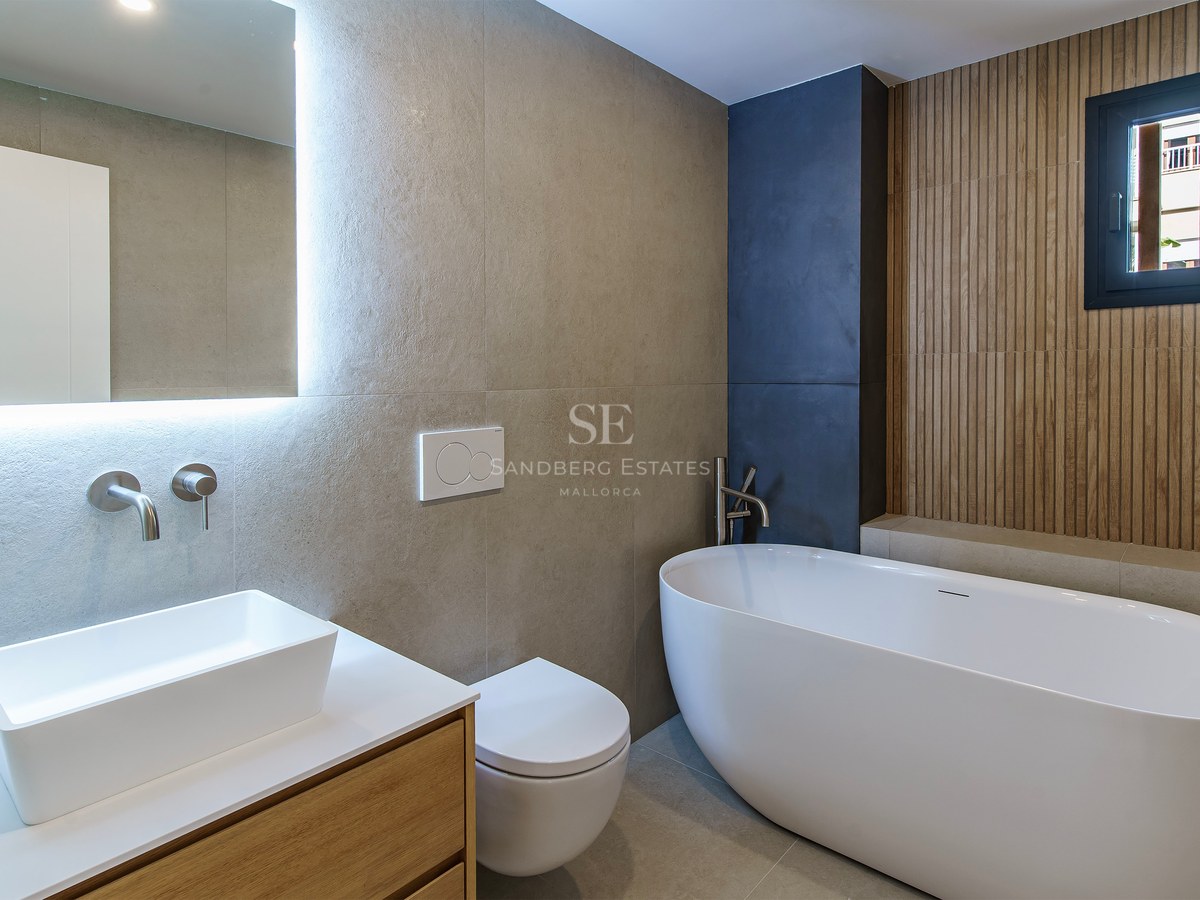 Modern bathroom featuring a freestanding oval tub, a white vessel sink on wood vanity, and a backlit mirror.