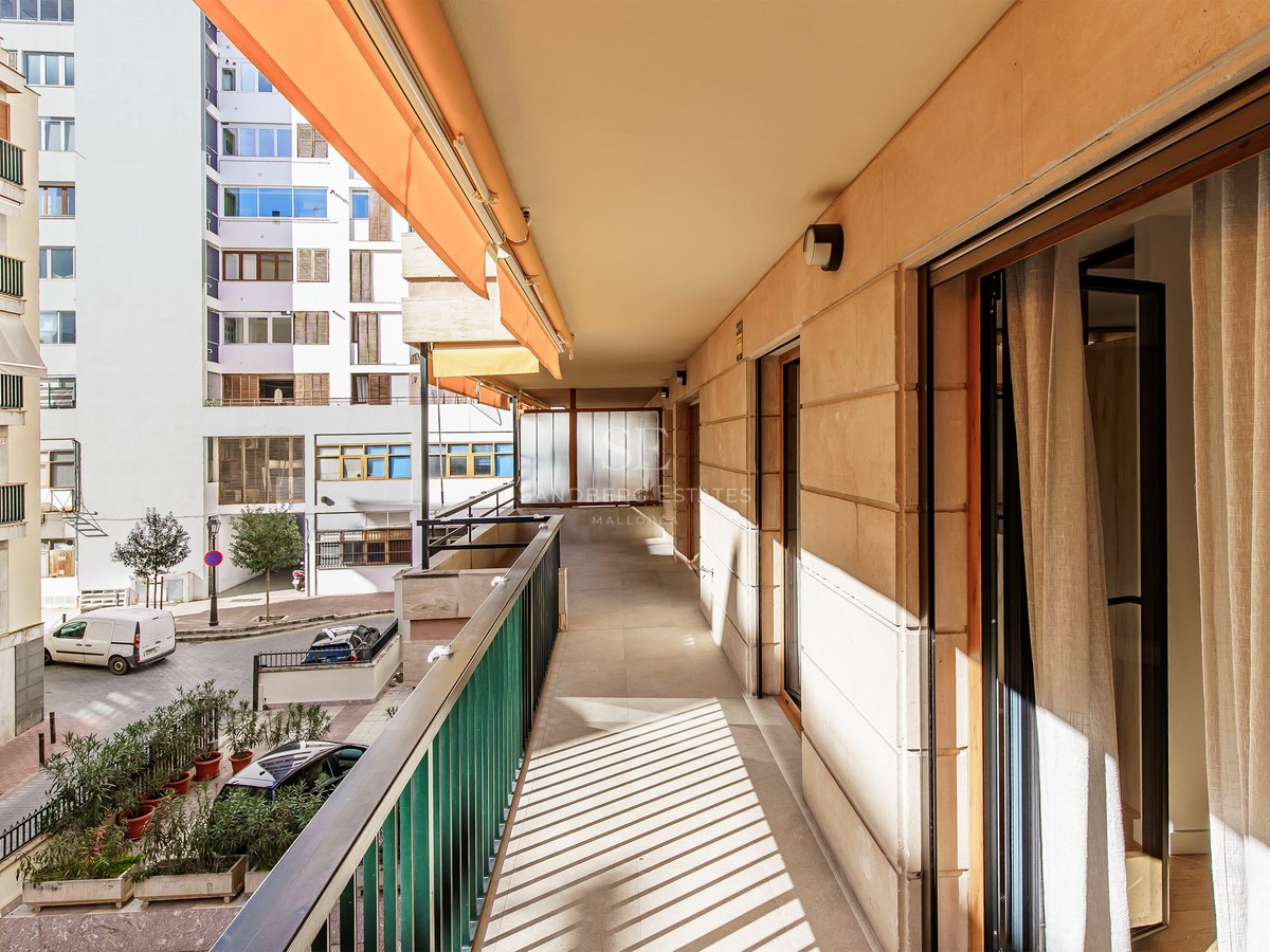 Long sunny balcony with orange awning and metal railing overlooking an urban street.