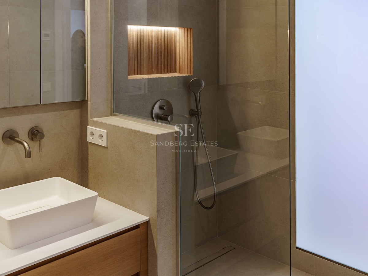 Modern bathroom featuring a white vessel sink, stone-tiled walls, and a glass walk-in shower with an illuminated wood niche.