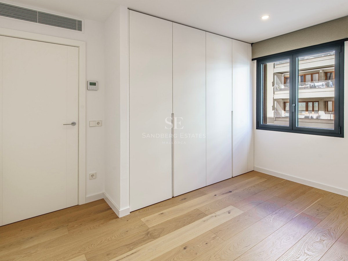 Bright room with light wood floors, large white built-in closets, a white door, and a window with a dark frame.