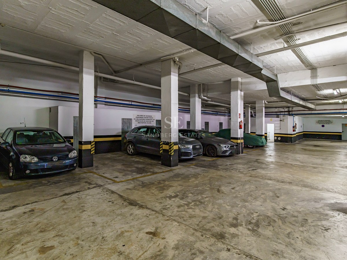 Spacious underground garage with concrete pillars, yellow safety markings, and parked cars.