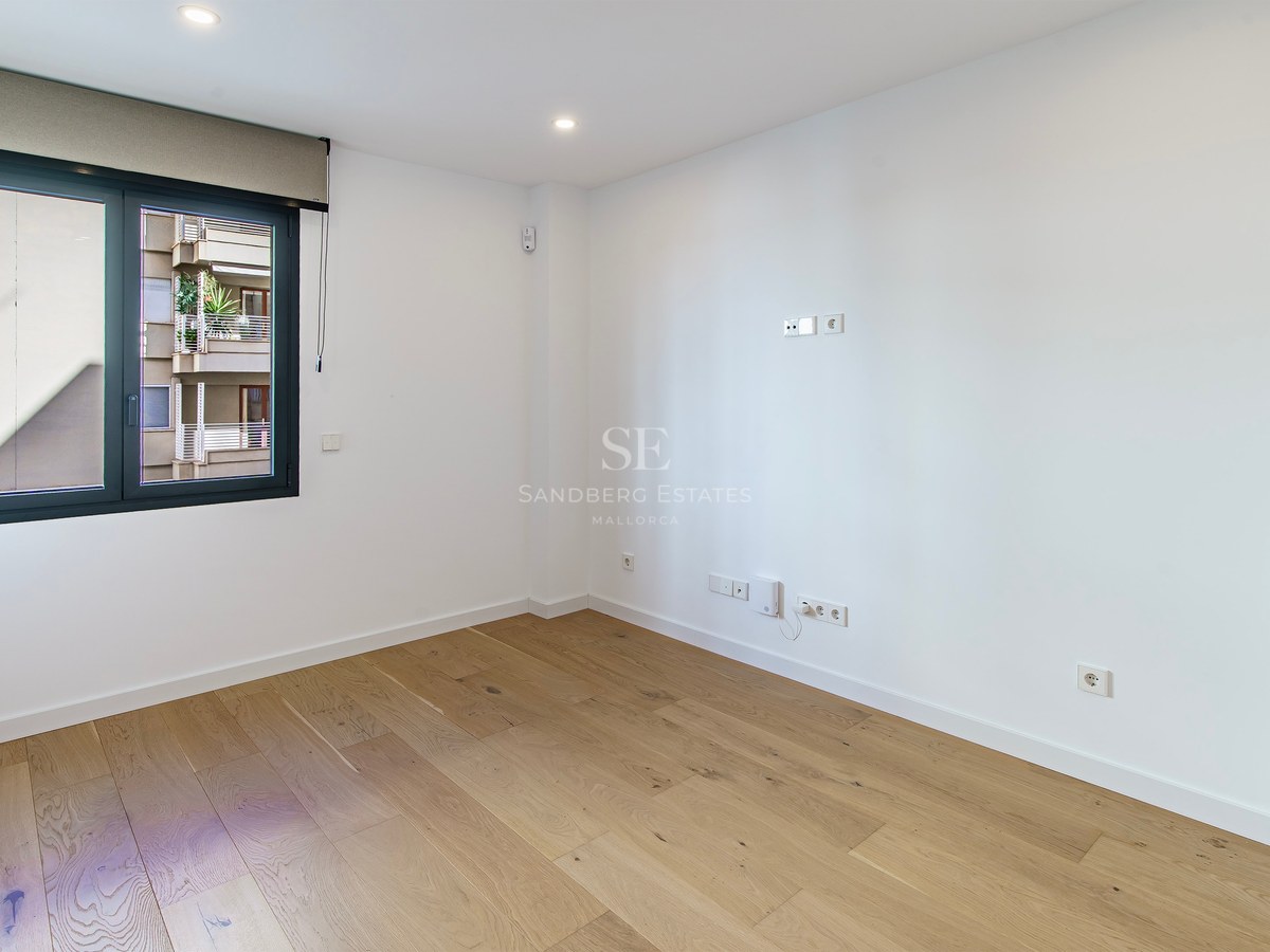 Bright empty room with light wood floors, white walls, and a large window with a roller blind.