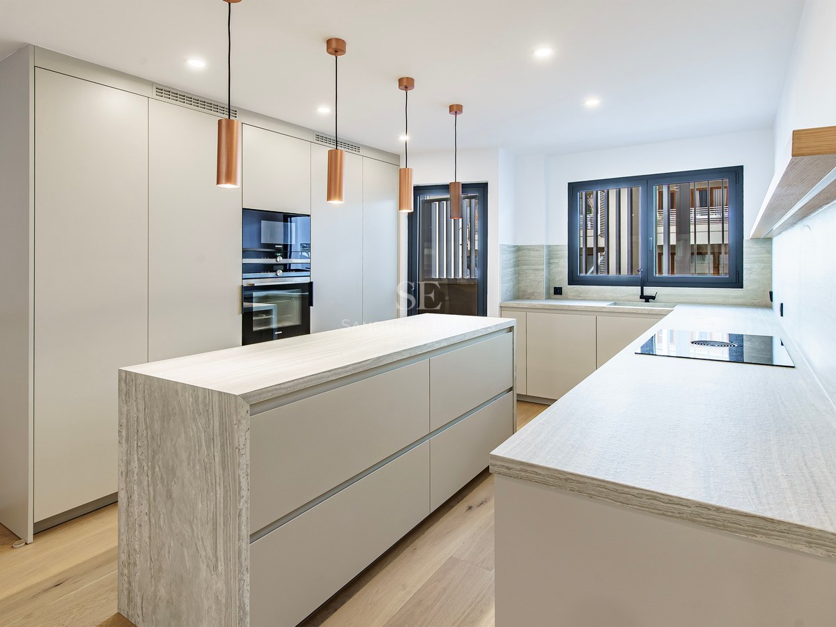 Contemporary white kitchen featuring a stone island, copper pendant lights, and wood flooring.