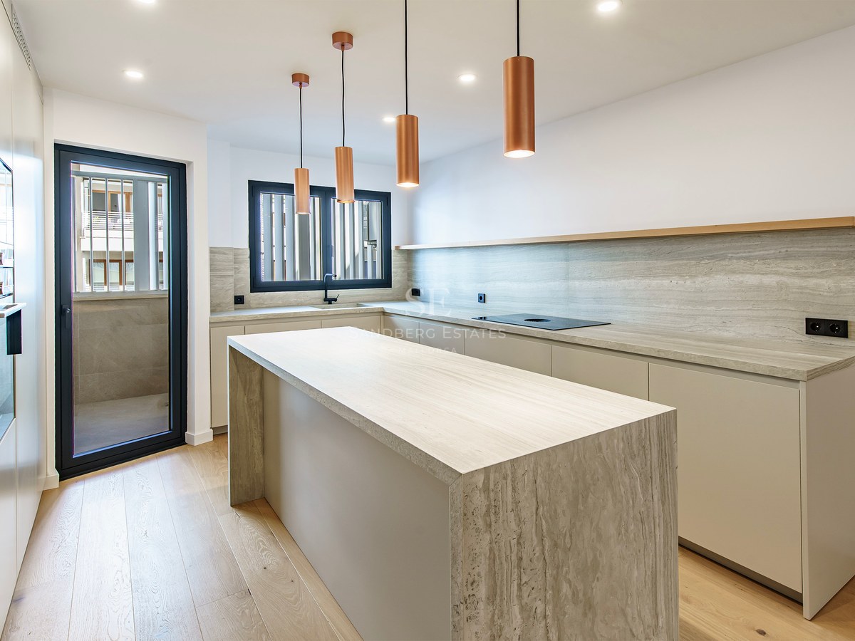 Bright kitchen featuring a large travertine stone island, copper pendant lights, and light wood flooring.