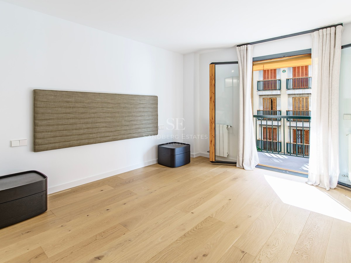 Modern bedroom with light wood floors, a textured wall-mounted headboard, and balcony doors with natural light.