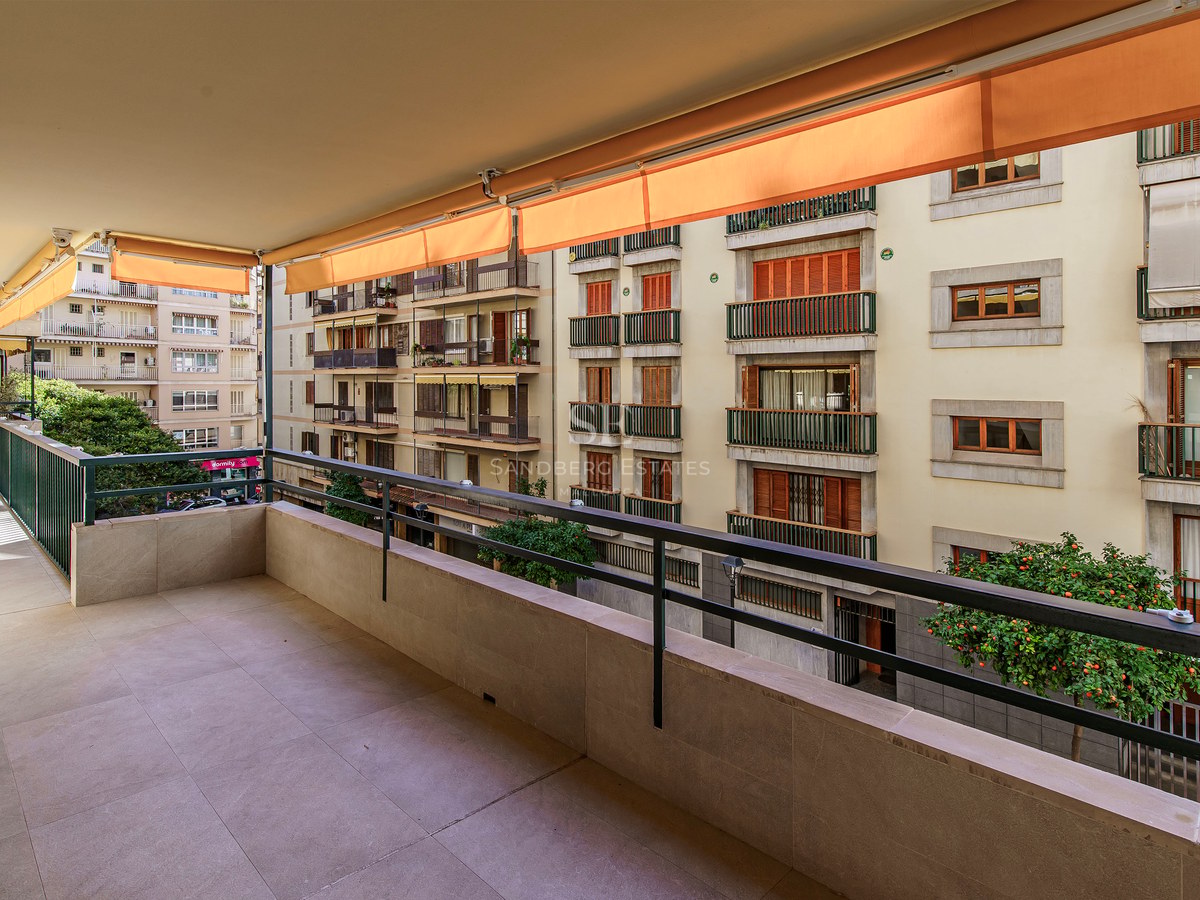 Wide stone terrace with metal railing and orange retractable awnings overlooking residential buildings.