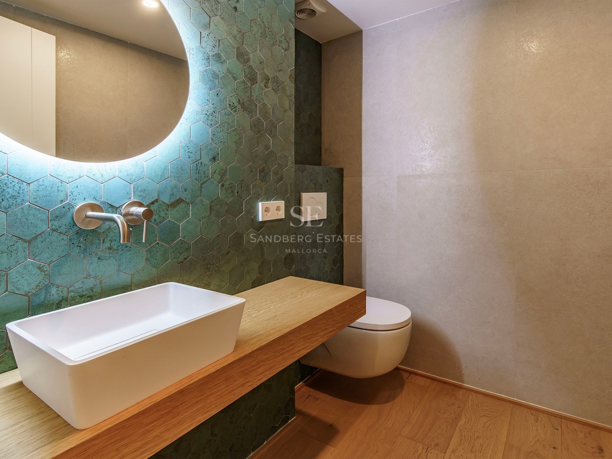 Modern bathroom featuring teal hexagonal tiles, a white vessel sink on a wooden vanity, and a large circular backlit mirror.