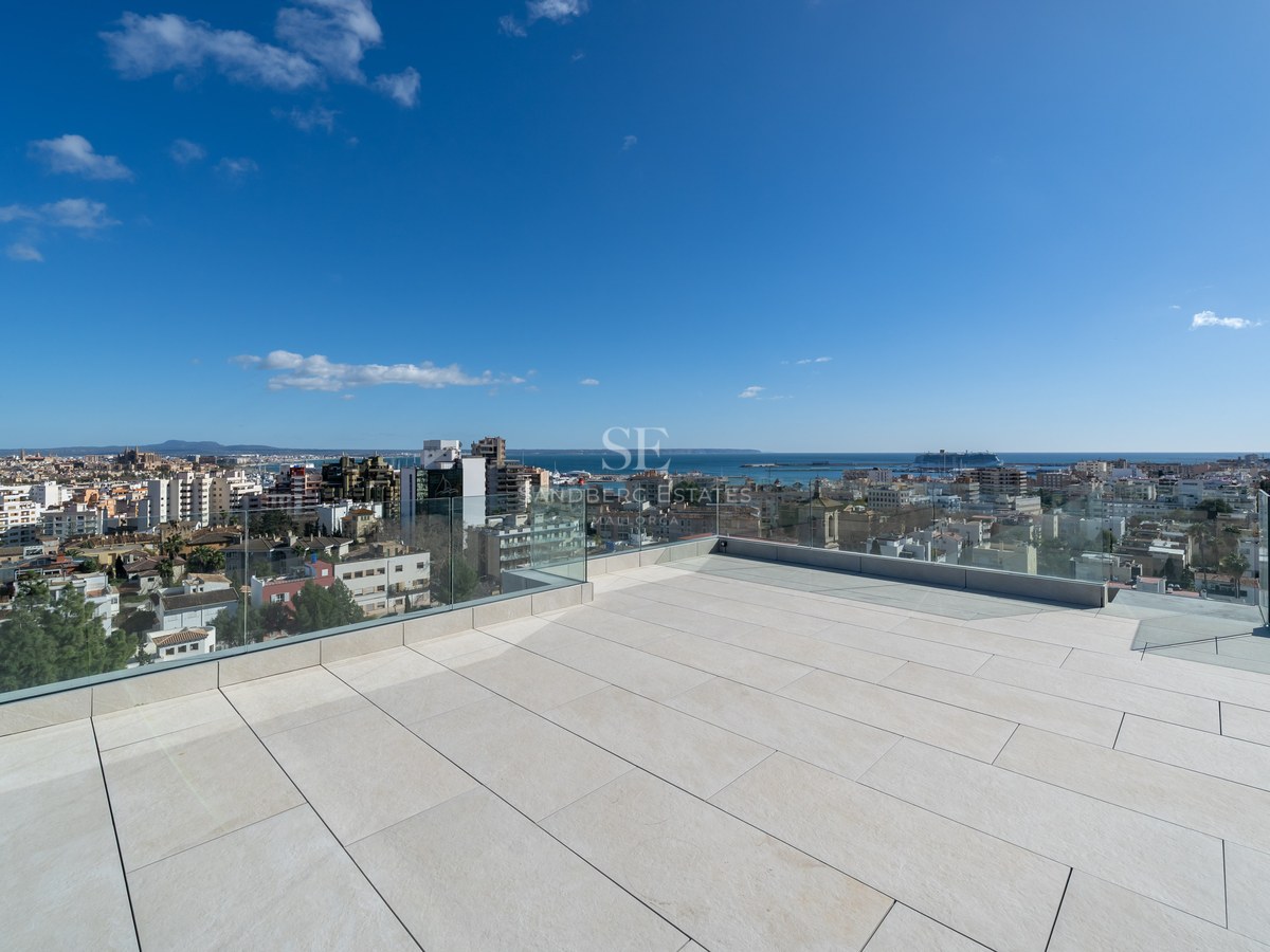 Stor takterrass med ljusa stenplattor och glasräcken med utsikt över Palma stad, katedralen och havet.