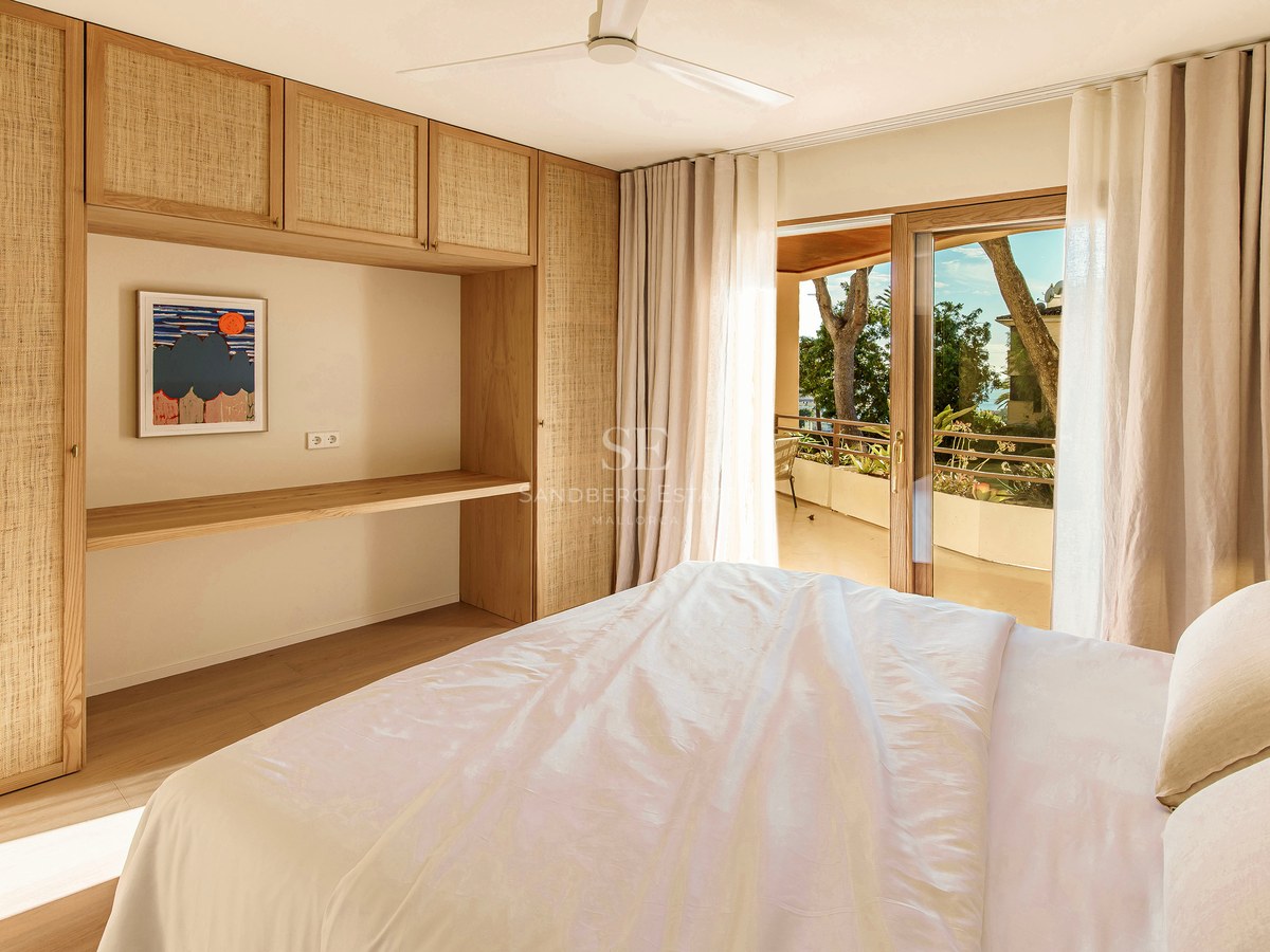 Helles Schlafzimmer mit Einbauschränken aus hellem Holz, Schreibtisch und Schiebetüren zu einer sonnigen Terrasse.