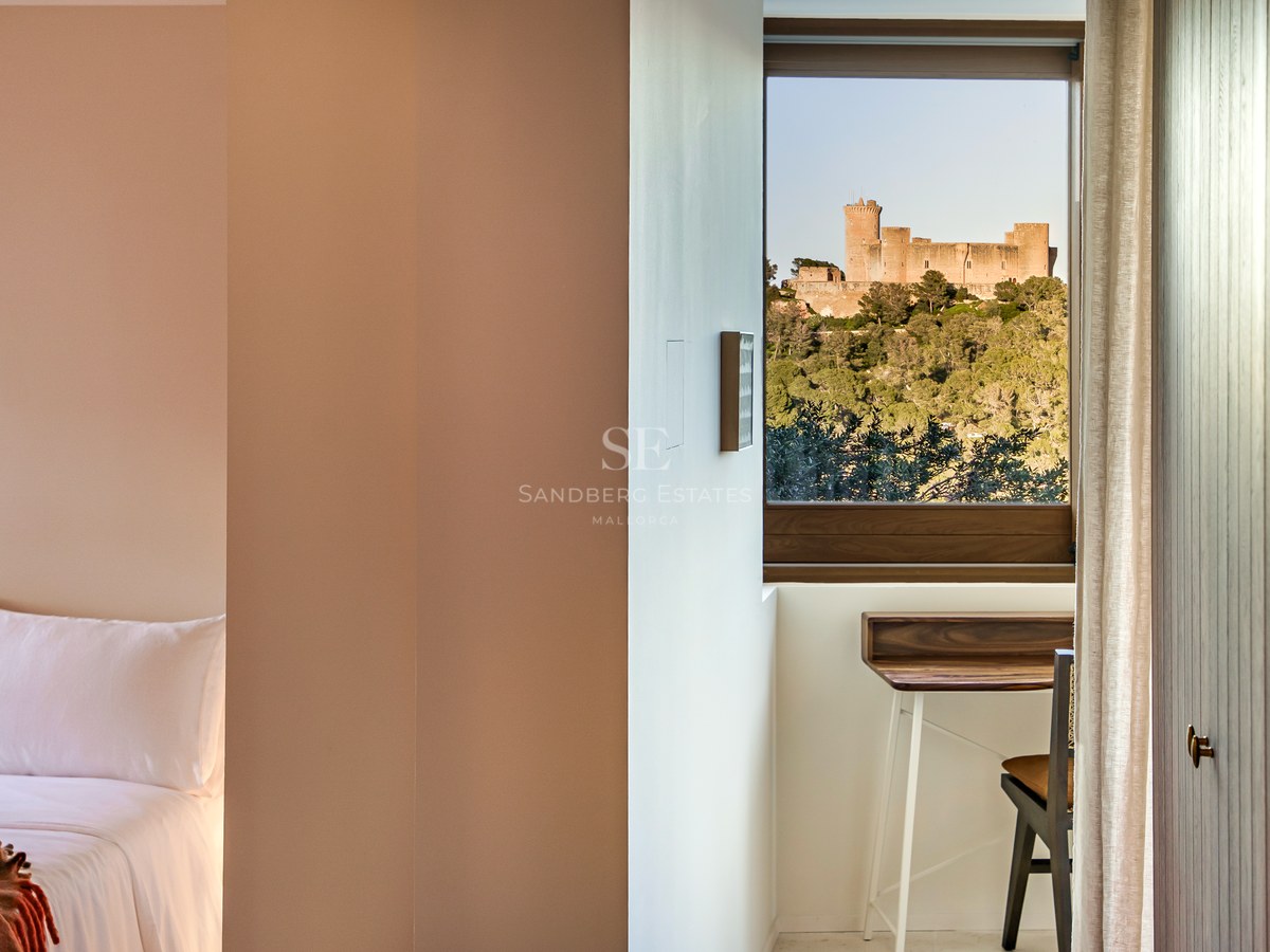 Modernes Schlafzimmerfenster mit Blick auf eine mittelalterliche Burg auf einem bewaldeten Hügel und einem Schreibtisch.