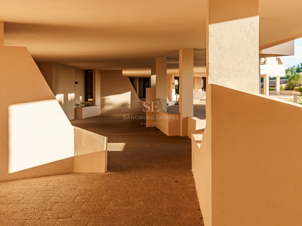 Schattiger Außenweg mit beigen geometrischen Wänden und Steinboden bei warmem Sonnenlicht und scharfen Schatten.
