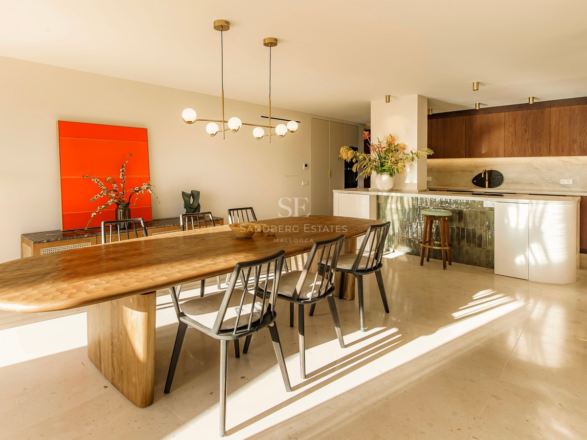 Großzügiges Esszimmer mit ovalem Holztisch, Designer-Pendelleuchte und moderner Küche im Hintergrund bei Sonnenlicht.