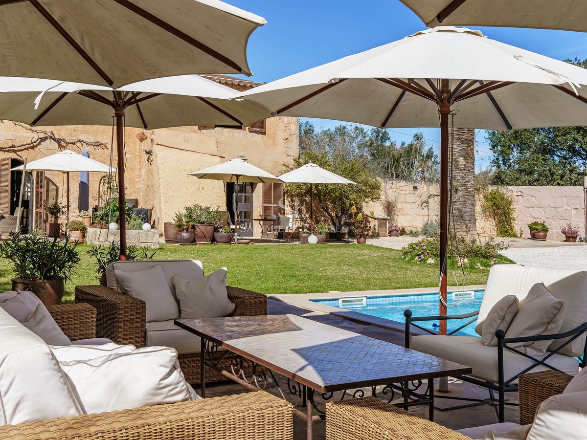 Schwimmbad umgeben von großen weißen Sonnenschirmen und Loungemöbeln aus Korbgeflecht in einem mediterranen Garten.
