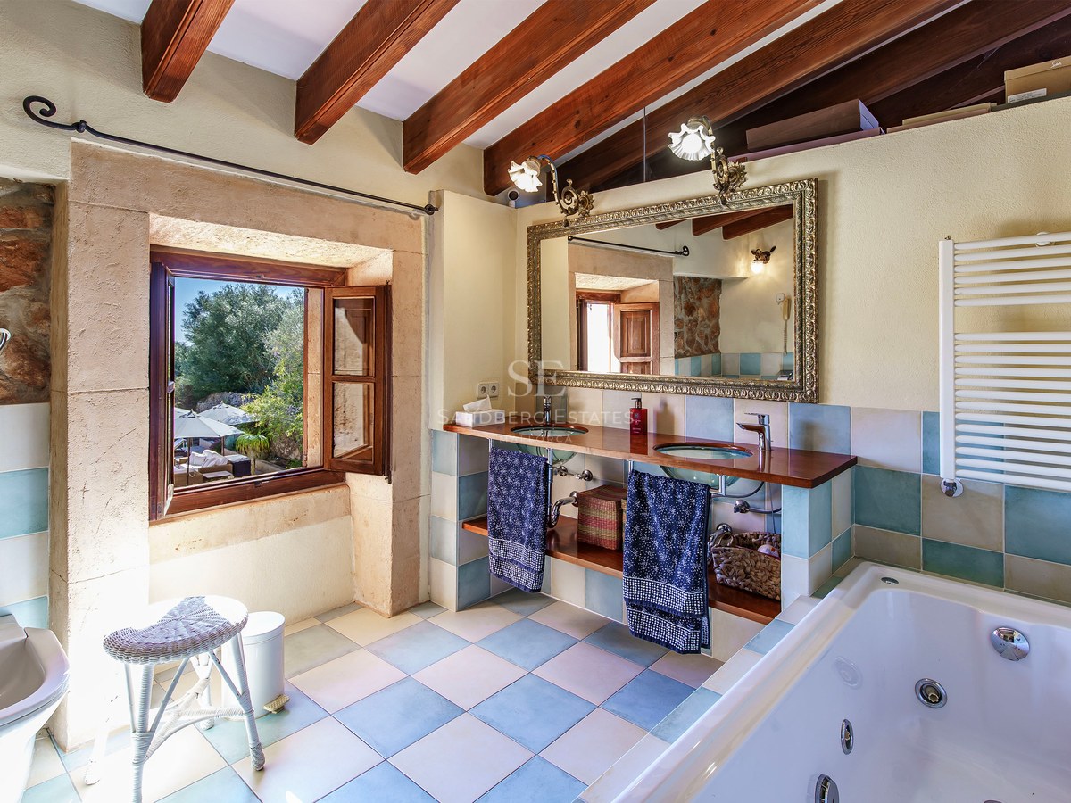 Hauptbadezimmer mit Holzbalken, Doppelwaschbecken aus Glas, Prunkspiegel und Whirlpool-Badewanne.