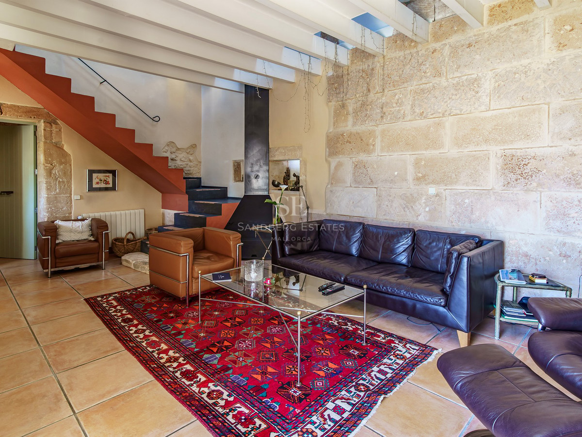 Wohnzimmer mit Ledersofas, rotem Teppich, Steinwand und Treppe mit Terrakotta-Akzenten.