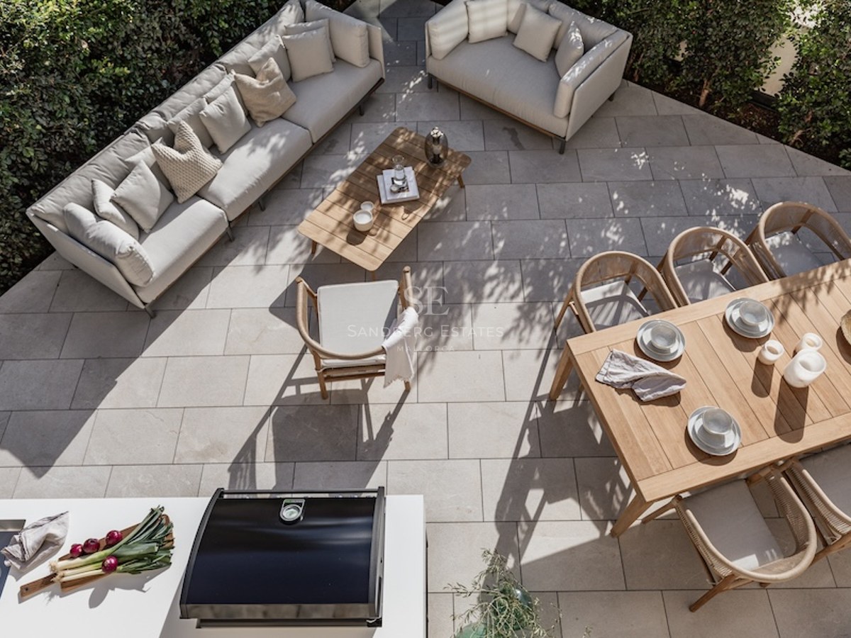 High-angle view of a stone-paved terrace with designer sofas, wooden dining table, and outdoor kitchen area.